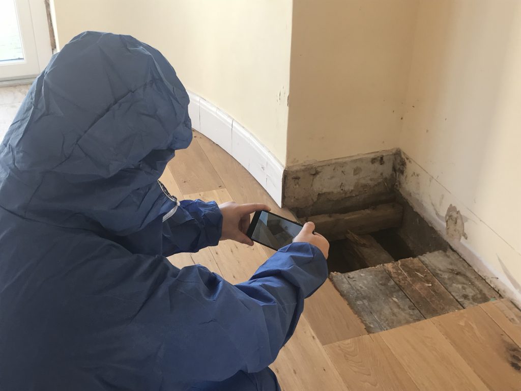 Man in Protective Blue Clothing Taking a picture of Problematic Flooring